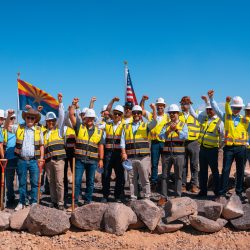 Project leaders, officials and construction partners in hard hats raising fists in celebration at the Project Sterling groundbreaking in Mohave County, Arizona