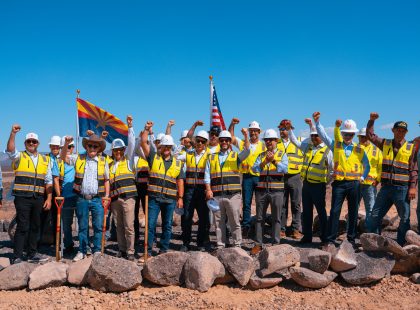 Project leaders, officials and construction partners in hard hats raising fists in celebration at the Project Sterling groundbreaking in Mohave County, Arizona