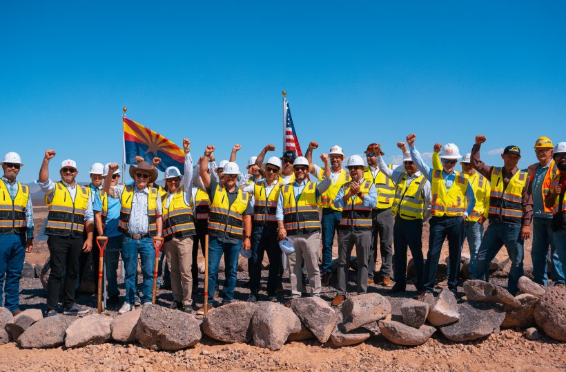 Project leaders, officials and construction partners in hard hats raising fists in celebration at the Project Sterling groundbreaking in Mohave County, Arizona
